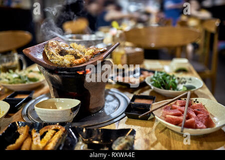 Le poisson grillé Steak et les crevettes sur le pot chaud avec la combustion du charbon sur la table en bois dans le café vietnamien. La nourriture variée sur les plaques sont autour de lui. Fermer Banque D'Images