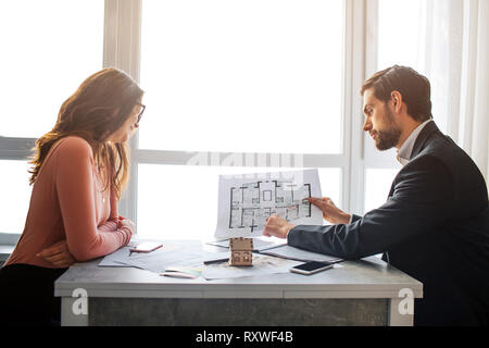 Couple acheter ou louer vacances ensemble. Jeune homme sérieux regarder en bas et point sur plan. Il commence avec le doigt. Femmes plus là aussi. S'asseoir à la fenêtre. Banque D'Images