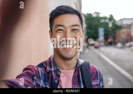 Smiling Young Asian man en tenant vos autoportraits sur une rue de la ville Banque D'Images