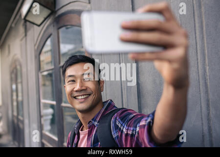 Young Asian man smiling tout en prenant vos autoportraits à l'extérieur Banque D'Images