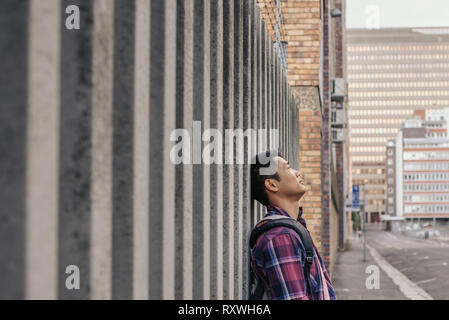 Content Young Asian man leaning against a wall Banque D'Images