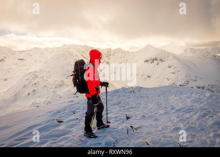 L'homme à la veste rouge, avec piolet randonnée / Escalade en hiver sur la montagne couverte de neige en Ecosse. Modèle libération - Garbh Bheinn, Highlands Loch Leven Banque D'Images