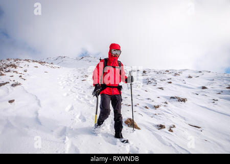 L'homme à la veste rouge, avec piolet randonnée / Escalade en hiver sur la montagne couverte de neige en Ecosse. Modèle libération - Garbh Bheinn, Highlands Loch Leven Banque D'Images