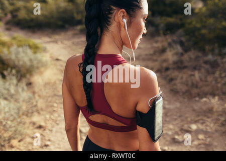 Vue arrière de l'ajustement jeune femme avec des écouteurs pour écouter de la musique avant de commencer son entraînement en cours d'exécution. Mettre en place avant de l'athlète féminine sa course sur sentier de montagne. Banque D'Images