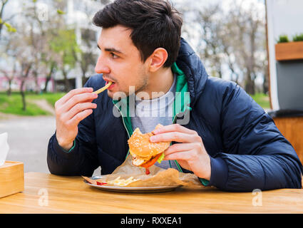 L'homme de manger des pommes de terre sautées avec un hamburger dans street food cafe Banque D'Images