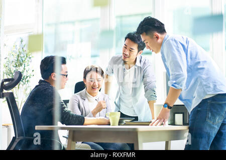 Groupe de quatre professionnels de jeunes dirigeants d'Asie qui travaillent ensemble en discutant affaires réunion bureau en bureau. Banque D'Images