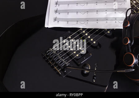 Note de musique, une prise casque et de guitare électrique sur fond noir. Banque D'Images