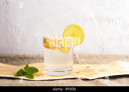 Verre avec l'eau de gingembre sur morceau d'écorce sur jute on white background. Banque D'Images