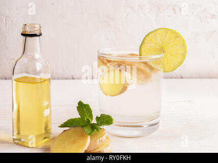 Verre avec l'eau de gingembre et une bouteille d'huile de gingembre sur tableau blanc sur fond clair. Banque D'Images