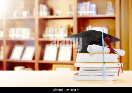 Graduation hat, faites défiler jusqu'à un diplôme et des livres sur la table avec étagère sur fond de bibliothèque Banque D'Images