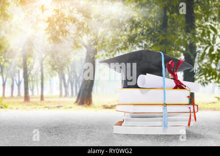 Graduation hat, faites défiler jusqu'à un diplôme et des livres sur la route avec des arbres et vue sur le parc sur fond de la lumière du soleil Banque D'Images