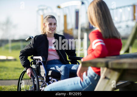 Teenage Girl In Wheelchair Talking With Friend In Park Banque D'Images