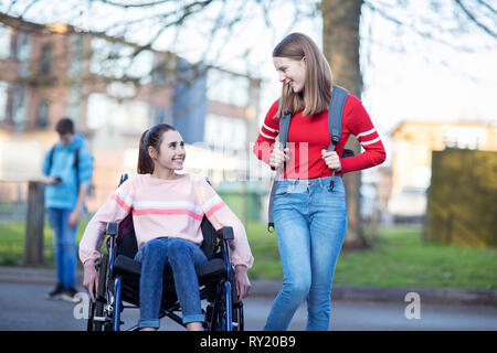 Teenage Girl In Wheelchair Talking With Friend comme ils quittent l'école secondaire Banque D'Images