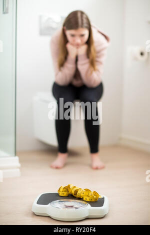 Malheureux Teenage Girl Sitting dans la salle de bains à la recherche, à des échelles et ruban à mesurer Banque D'Images