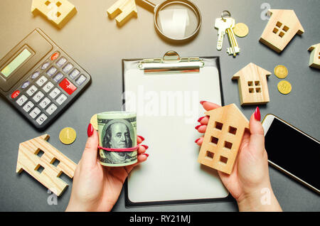 Une jeune fille tient dans ses mains un dollars et une maison miniature. Le concept d'évaluation des risques pour l'achat de biens immobiliers. Attirer les investissements dans le pr Banque D'Images