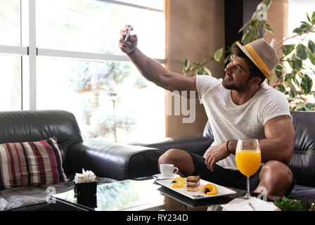 Happy Young Man Sitting on Sofa détendue au bar du hall de l'hôtel de luxe et de prendre un téléphone avec Selfies Banque D'Images