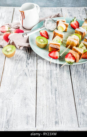 Petit-déjeuner d'été en-cas. Brochettes de fruits dessert vegan en brochettes avec du pain grillé français de pain frit, des fruits et des baies. Avec du sucre en poudre et le chocolat sau Banque D'Images