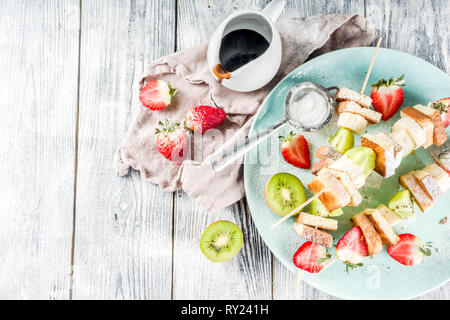 Petit-déjeuner d'été en-cas. Brochettes de fruits dessert vegan en brochettes avec du pain grillé français de pain frit, des fruits et des baies. Avec du sucre en poudre et le chocolat sau Banque D'Images