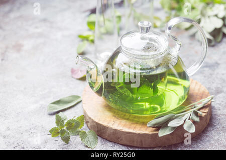 Sex herbal sédatif le thé à la menthe verre dans une théière en verre sur plateau en bois avec des feuilles de sauge et menthe du jardin sur fond gris Banque D'Images