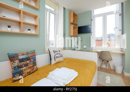 Petit appartement coloré dispose d''une chambre avec lit simple, de grandes fenêtres et un bureau avec chaise Banque D'Images