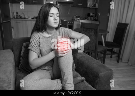 Jeune femme a une douleur au genou, photo en noir et blanc rouge Banque D'Images