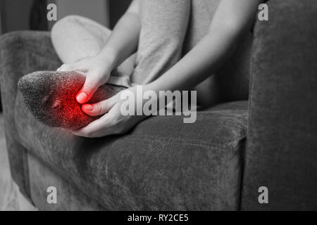 La douleur dans le pied, girl détient ses pieds, massage des pieds, crampes, spasmes musculaires, close-up photo en noir et blanc, rouge Banque D'Images