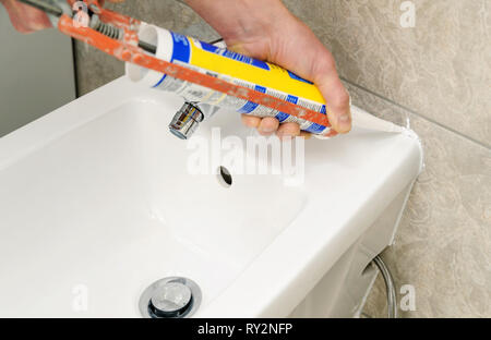 Worker met joint silicone de calfeutrer le joint entre bidet et le mur. Banque D'Images