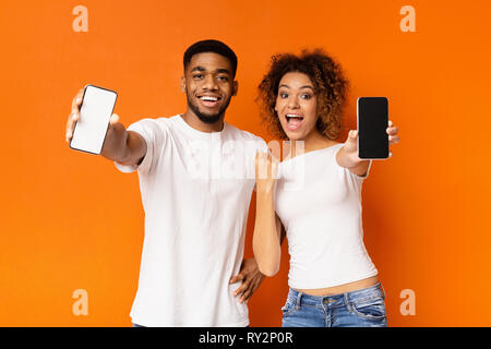 Cheerful black couple showing blank de smartphones Banque D'Images