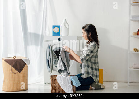 Femme en chemise grise et un jean enfiler ses vêtements dans le panier près de la rondelle dans la buanderie Banque D'Images