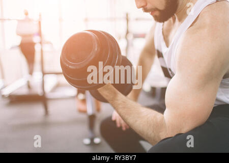 Homme barbu musculaire au cours de l'exercice dans la salle de sport. Bodybuilder musculaire de l'athlète dans la salle de fitness training biceps avec haltère. Remise en forme à l'intérieur Banque D'Images