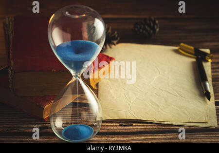 Hourglass et de vieux livres avec de vieux papier et stylo sur des tables en bois dans l'éclairage de la lanterne. Banque D'Images