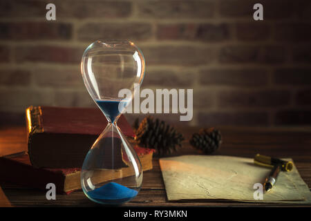 Hourglass et de vieux livres avec de vieux papier et stylo sur des tables en bois dans l'éclairage de la lanterne. Banque D'Images