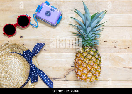 Mise à plat avec des feuilles vertes Ananas et lunettes de soleil, appareil photo, chapeau sur la texture background en bois. Vue d'en haut. Banque D'Images