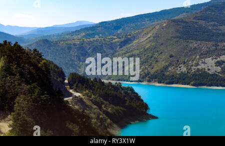 Route serpente à travers les Alpes françaises, à côté d'un lac bleu intense, haut dans les montagnes. Banque D'Images