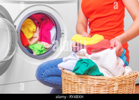 Jeune femme charge le linge dans la machine à laver du panier à linge avant de le laver. Banque D'Images