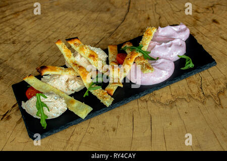 Apéritif de bretzels croustillants au sésame, deux types de caviar d'taramа, roquette et tomates cerises, servi sur un plateau noir sur un fond de bois. Banque D'Images