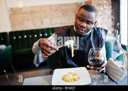 African man in black vêtements traditionnels et de manger des pâtes et boire du vin. Banque D'Images