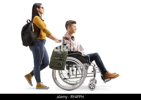 Profil de pleine longueur tourné d'une étudiante en poussant un élève dans un fauteuil roulant isolé sur fond blanc Banque D'Images