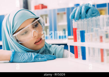 Femme scientifique musulmane à la recherche de tubes à essai avec un liquide rouge et bleu in lab Banque D'Images