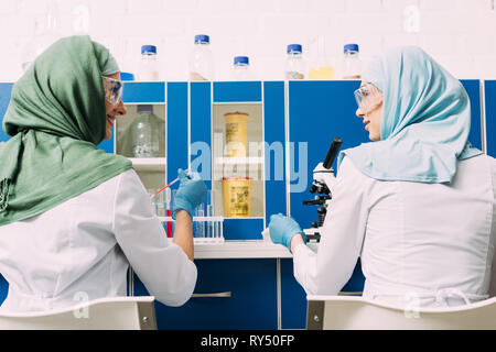 Vue arrière de femmes scientifiques musulmans à la pipette et microscope en laboratoire de chimie Banque D'Images