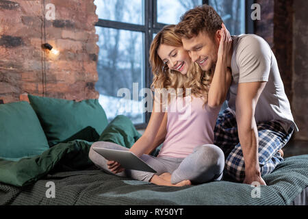 Heureux couple wearing pajamas regarder film sur tablet sitting in bed Banque D'Images