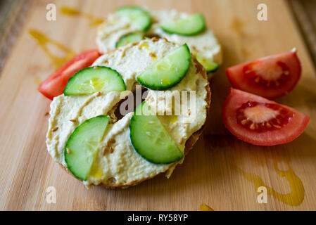 Un bagel avec du hoummos, humous, hommous et concombre, végétalien, végétarien, petit déjeuner ou déjeuner d'aliments sains sur une planche en bois Banque D'Images