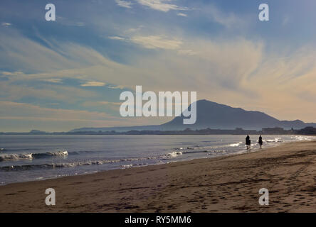 Rouleau de vagues sur une plage de sable fin aux cavaliers. La formation de nuages sur les montagnes et la plage de Méditerranée près de Denia, Valence, Espagne. Banque D'Images