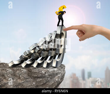Homme portant le signe du dollar en or, en équilibre sur la chute de l'Euro Currency Symbols avec big woman index aidant sur falaise, avec sun ciel cityscape Banque D'Images