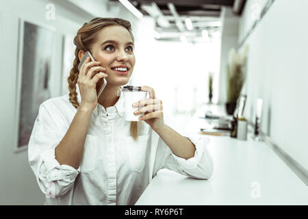 Sourire pensif dame exerçant son téléphone mobile et sirotant du café Banque D'Images
