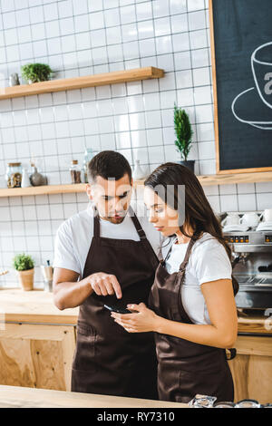 Les caissiers dans les tabliers brun debout derrière comptoir bar et à la maison de café pour smartphone dans Banque D'Images