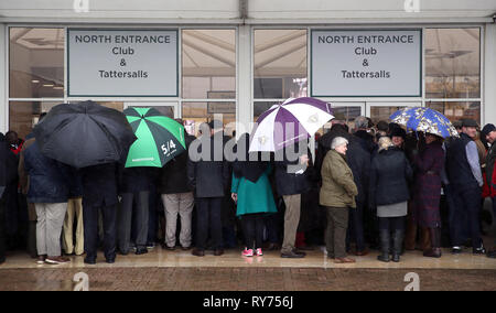 Racegoers abri de la pluie pendant qu'ils attendent pour les portes à ouvrir pour défendre jour de la Cheltenham Festival 2019 à l'Hippodrome de Cheltenham. Banque D'Images