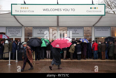 Racegoers abri de la pluie pendant qu'ils attendent pour les portes à ouvrir pour défendre jour de la Cheltenham Festival 2019 à l'Hippodrome de Cheltenham. Banque D'Images