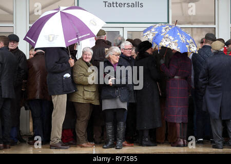 Racegoers abri de la pluie pendant qu'ils attendent pour les portes à ouvrir pour défendre jour de la Cheltenham Festival 2019 à l'Hippodrome de Cheltenham. Banque D'Images