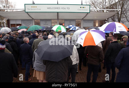 Racegoers abri de la pluie pendant qu'ils attendent pour les portes à ouvrir pour défendre jour de la Cheltenham Festival 2019 à l'Hippodrome de Cheltenham. Banque D'Images